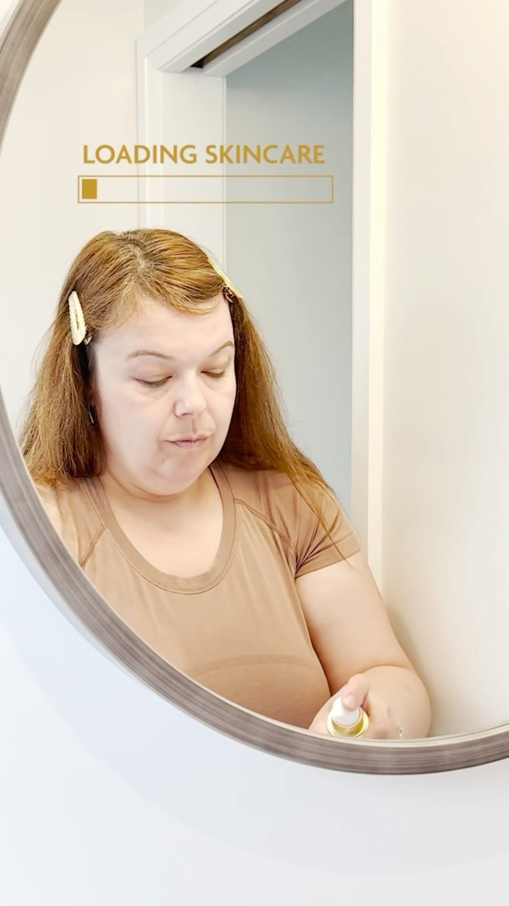 Woman stands in front of a mirror showing application of Goldie Lux 24 Karat Colloidal Gold products.