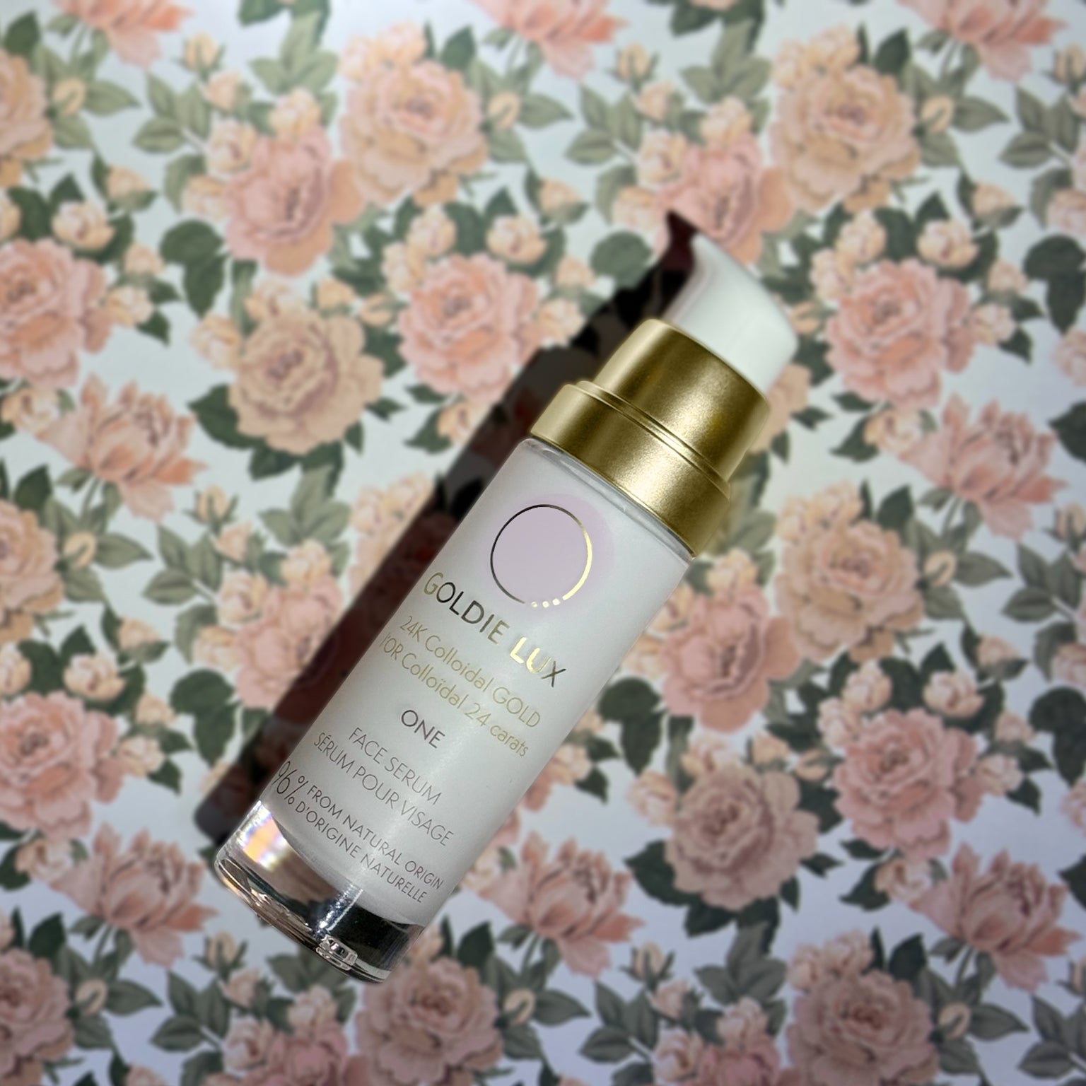 Goldie Lux | 24 Karat Colloidal Gold Face Serum glass bottle shown on a surface with a pink rose pattern.